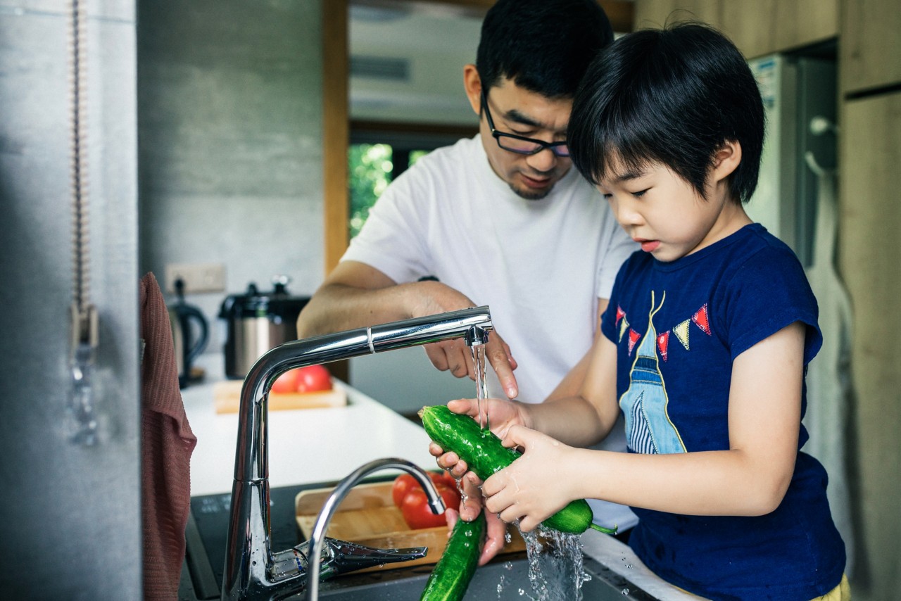 child and parent washing vegetables under the sink